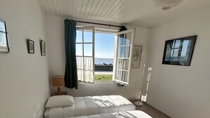 Une chambre à coucher avec un grand lit, une fenêtre avec des rideaux, une lampe et un tableau encadré au mur.