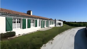 Un bâtiment blanc avec des volets verts, une petite dépendance attenante et un ciel dégagé.