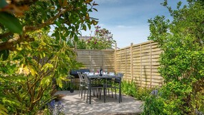 Un patio con mesa y sillas, rodeado de abundante vegetación y una valla de madera.