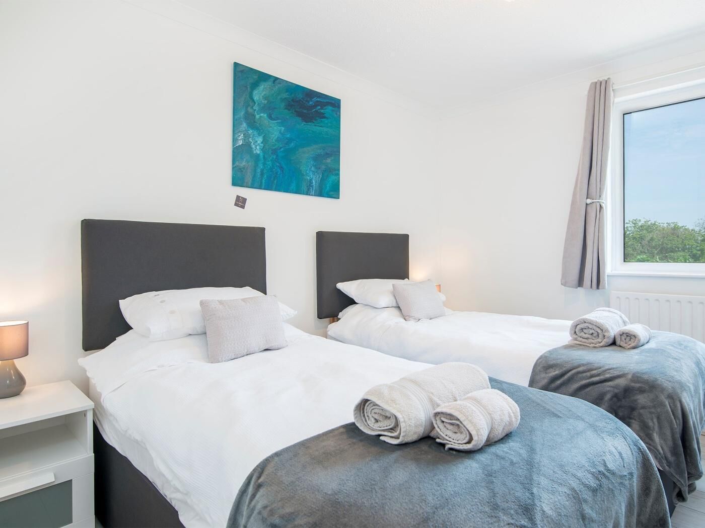 Una habitación de hotel con dos camas, un cuadro en la pared y una ventana con cortinas.