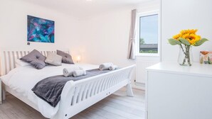 Un dormitorio con cama, mesita de noche, ventana con cortinas, radiador y un cuadro en la pared.