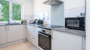 Una cocina moderna con armarios blancos, un horno Bosch, un microondas Comfoe y una ventana con vistas al verdor.