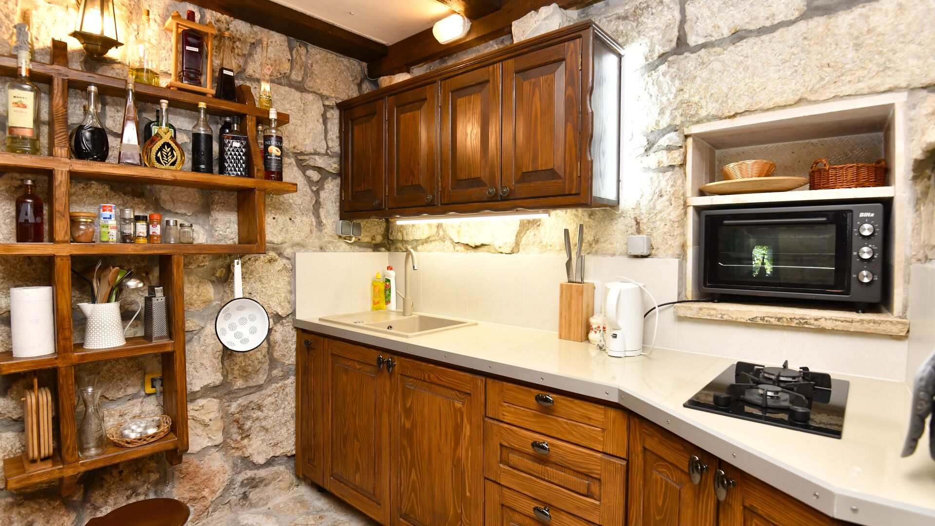 A kitchen with wooden cabinets, a stone wall, a microwave, and various kitchen utensils.