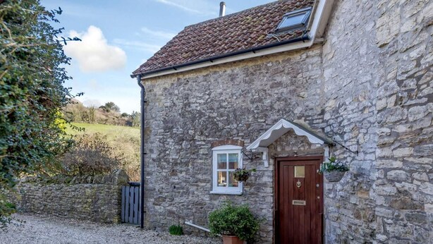A stone building with a wooden door, a window with a hanging plant, and a gravel driveway. - 3 Bed in Weymouth (oc-87065) (Weymouth)