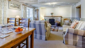 A cozy living room with a fireplace, striped sofas, a dining table with oranges and glasses, and a wooden ceiling. - 3 Bed in Weymouth (oc-87065) (Weymouth)