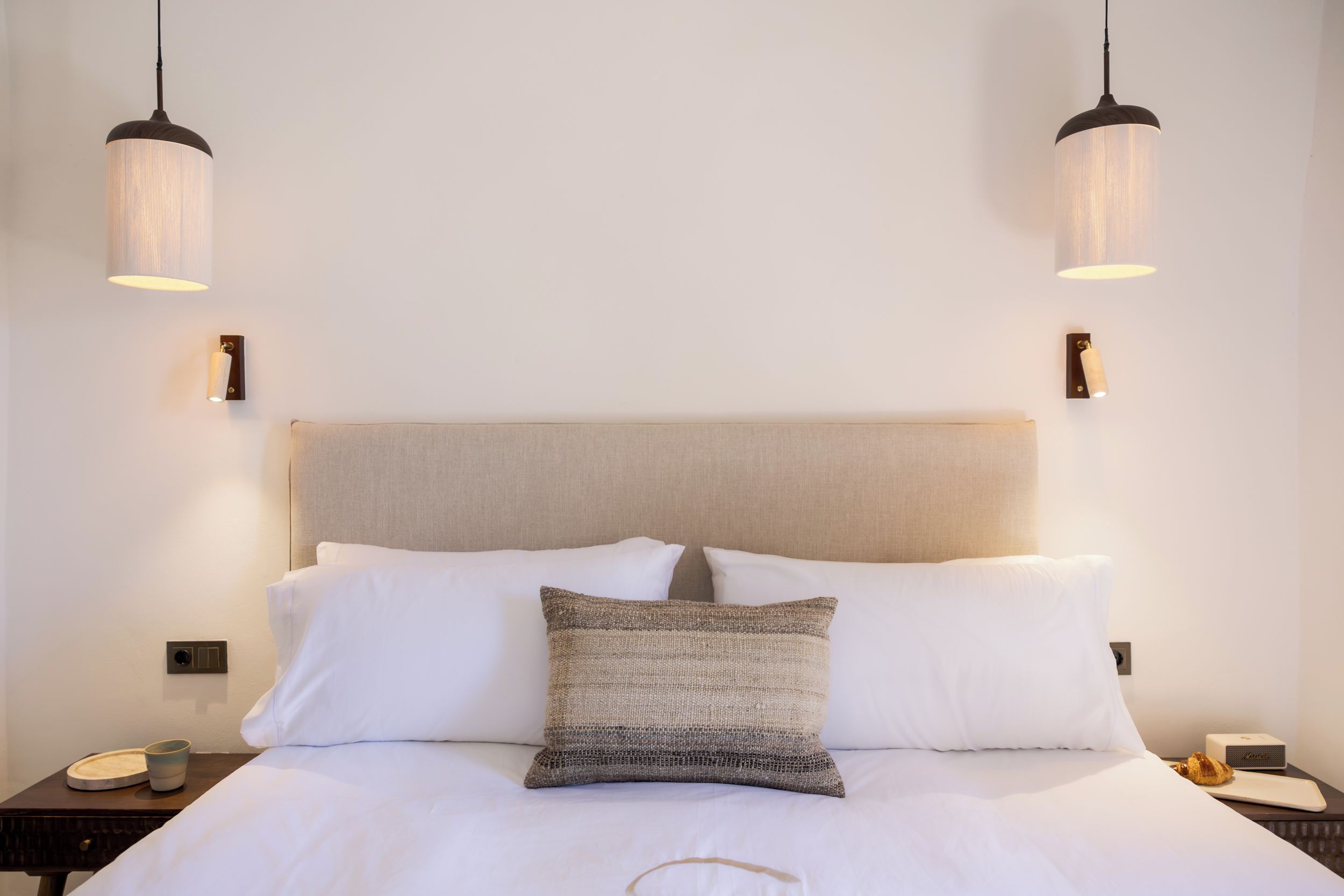 A hotel room with a bed, two bedside tables, a nightstand, a lamp, and a wall-mounted light fixture.