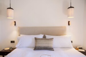 Una habitación de hotel con cama, dos mesitas de noche, lámpara y luz empotrada en la pared.