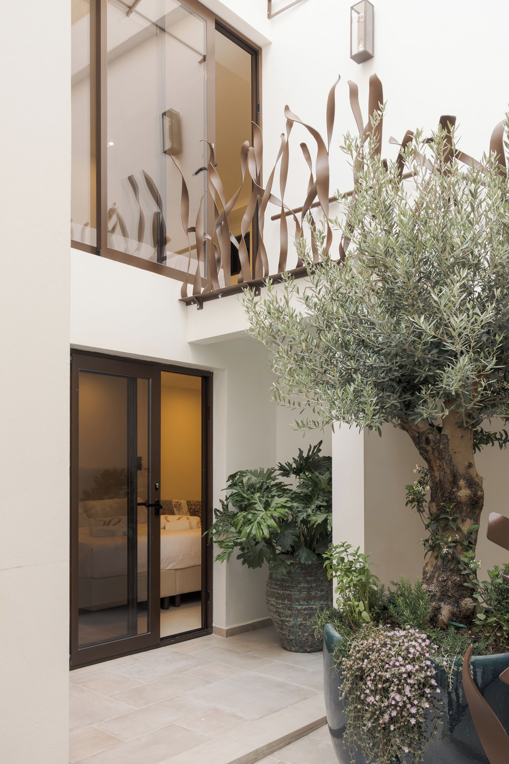 Un moderno vestíbulo de hotel con puerta de cristal, una gran planta en maceta y una escultura de metal decorativa.