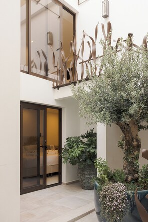 Un moderno vestíbulo de hotel con puerta de cristal, una gran planta en maceta y una escultura de metal decorativa.