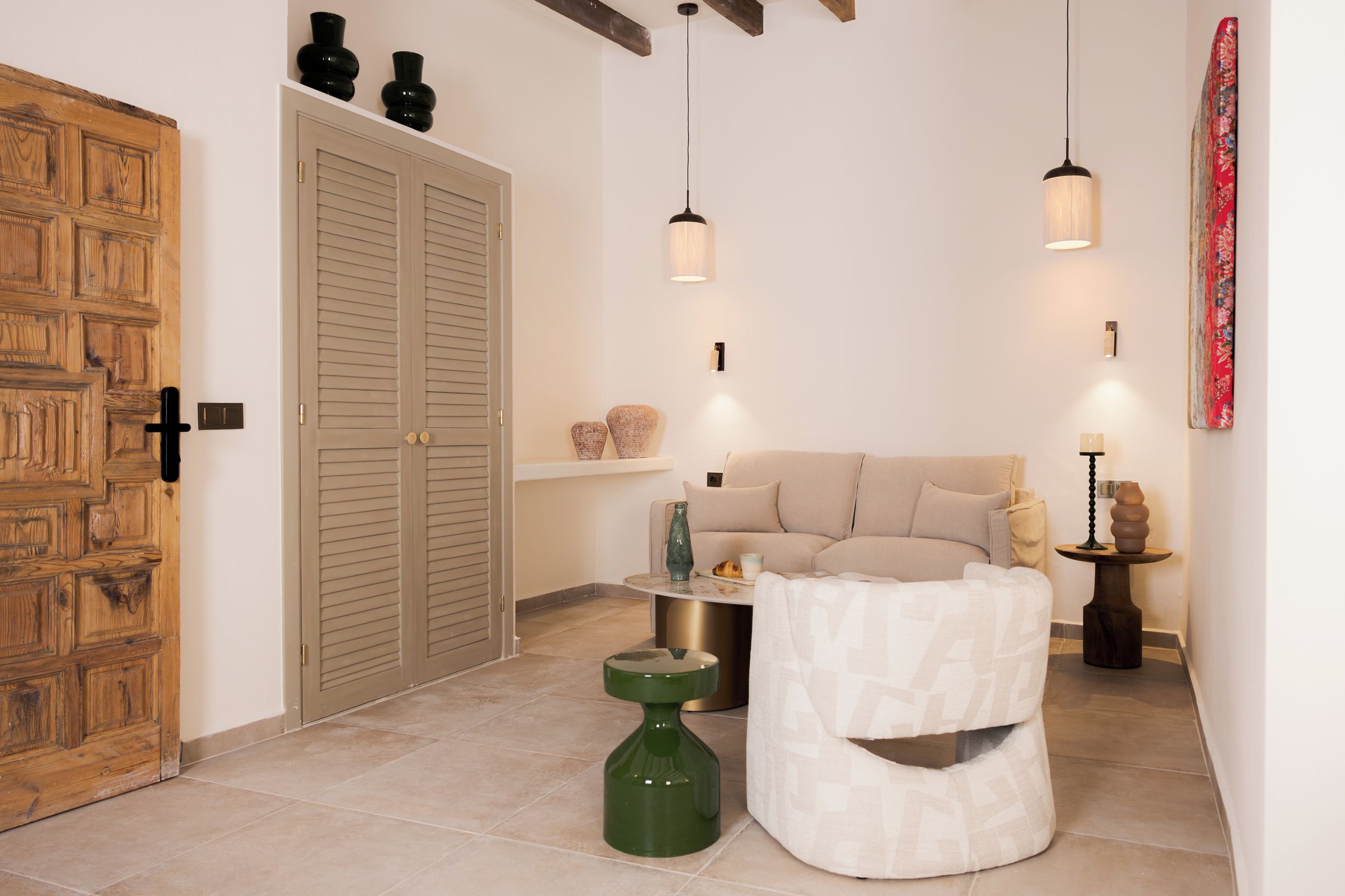 Una habitación con puerta de madera, un sofá color beige, una mesita y una botella verde.