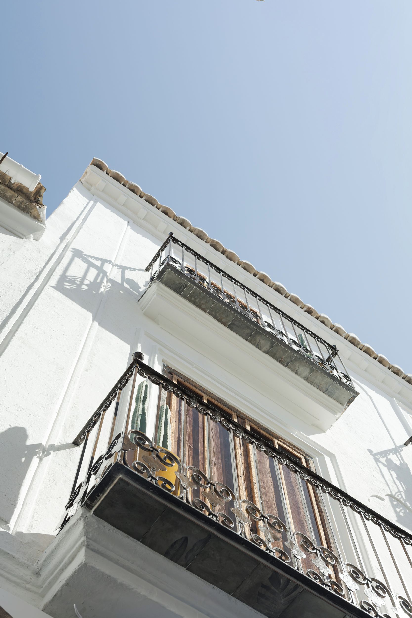 Un edificio blanco con un balcón que tiene barandilla de hierro forjado y un objeto amarillo pequeño en la parte inferior.