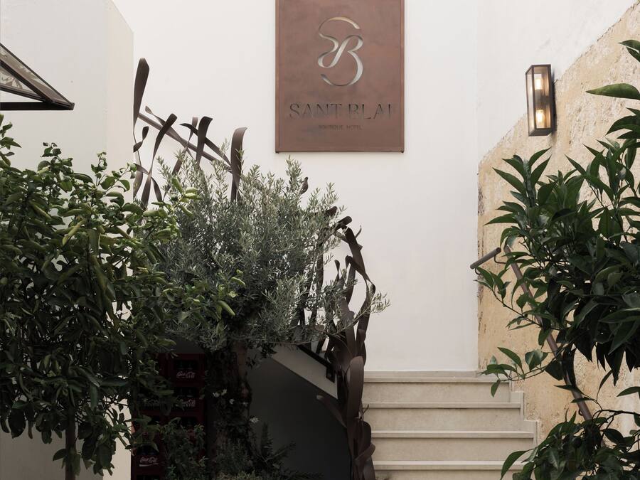 A staircase with a sign above it, surrounded by potted plants and a wall-mounted light fixture.