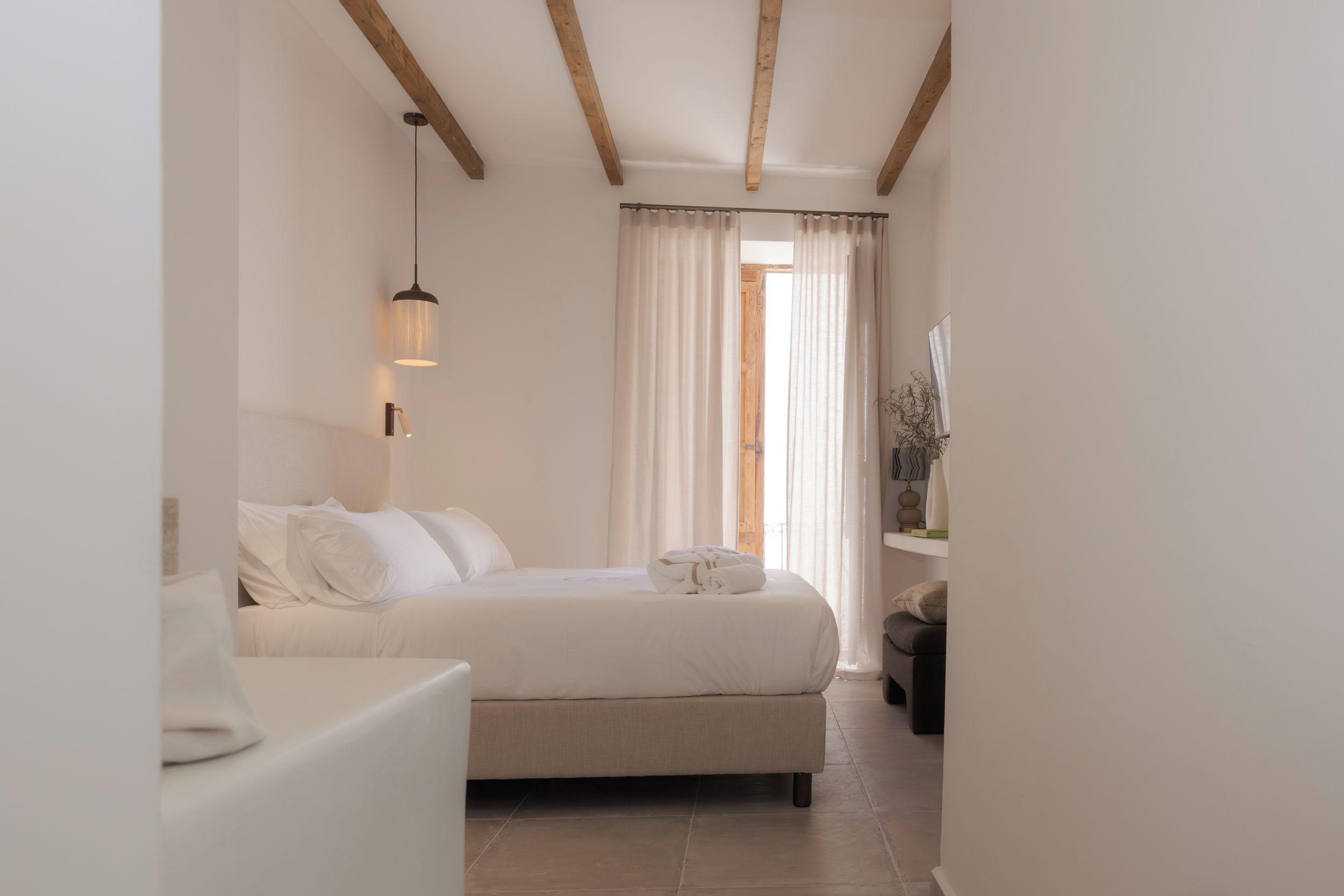 A bedroom with a bed, bedside table, and a hanging light fixture.