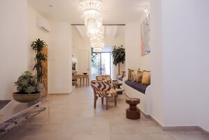 Un amplio pasillo con candelabro, zona de estar con sillas estampadas y plantas en macetas.
