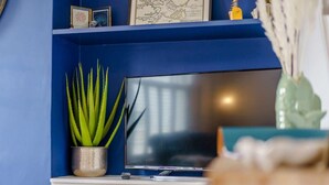 Ein Zimmer mit blauer Wand, einem Flachbildfernseher auf einem weißen Schrank und einem Topf mit Aloe-Pflanze.