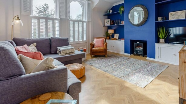 Ein Wohnzimmer mit Sofa, Sesseln, Hocker und Kamin.