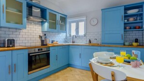 Eine Küche mit blauen Schränken, einer Holztischplatte, einem weißen Esstisch und einem Fenster.