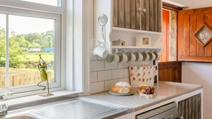Eine Küche mit Fenster, Spüle, einer Arbeitsfläche mit Brot und Trauben sowie einem Holzschrank mit dekorativem Spiegel.