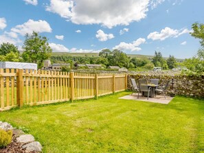 A fenced backyard with a table and chairs, stone wall, and a view of houses and hills in the background. - 2 Bed in Skipton (oc-87370) (Kettlewell)