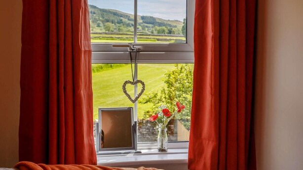 Ein Fenster mit roten Vorhängen, einer herzförmigen Dekoration und einer Blumenvase.