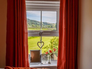 A window with red curtains, a heart-shaped decoration, and a vase with flowers. - 2 Bed in Skipton (oc-87370) (Kettlewell)