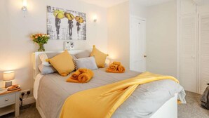 Ein ordentlich bezogenes Bett in Grau und Gelb, ein Wandbild und eine Nachttischlampe.