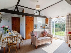 A cozy room with a dining table set for breakfast, a sofa with plaid cushions, and a view of the garden through a glass door. - 1 Bed in Norwich (oc-87414) (Hainford)