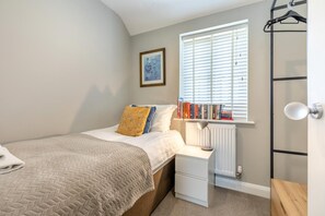 A bedroom with a bed, a bedside table with a lamp, a radiator, a window with blinds, and a wall-mounted shelf with books. - 3 Bed in Marston Montgomery (oc-87450) (Marston Montgomery)