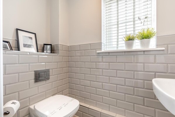 A bathroom with a toilet, a shelf with framed pictures, and a window with plants. - 3 Bed in Marston Montgomery (oc-87450) (Marston Montgomery)
