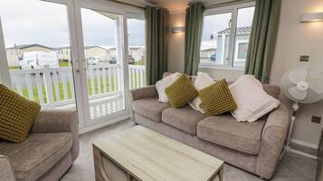 A living room with a sofa, a coffee table, and a fan. There is a sliding glass door leading to a balcony.