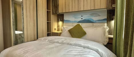 Un grand lit recouvert d’une courtepointe matelassée, un oreiller vert et un tableau représentant un phare accroché au mur.