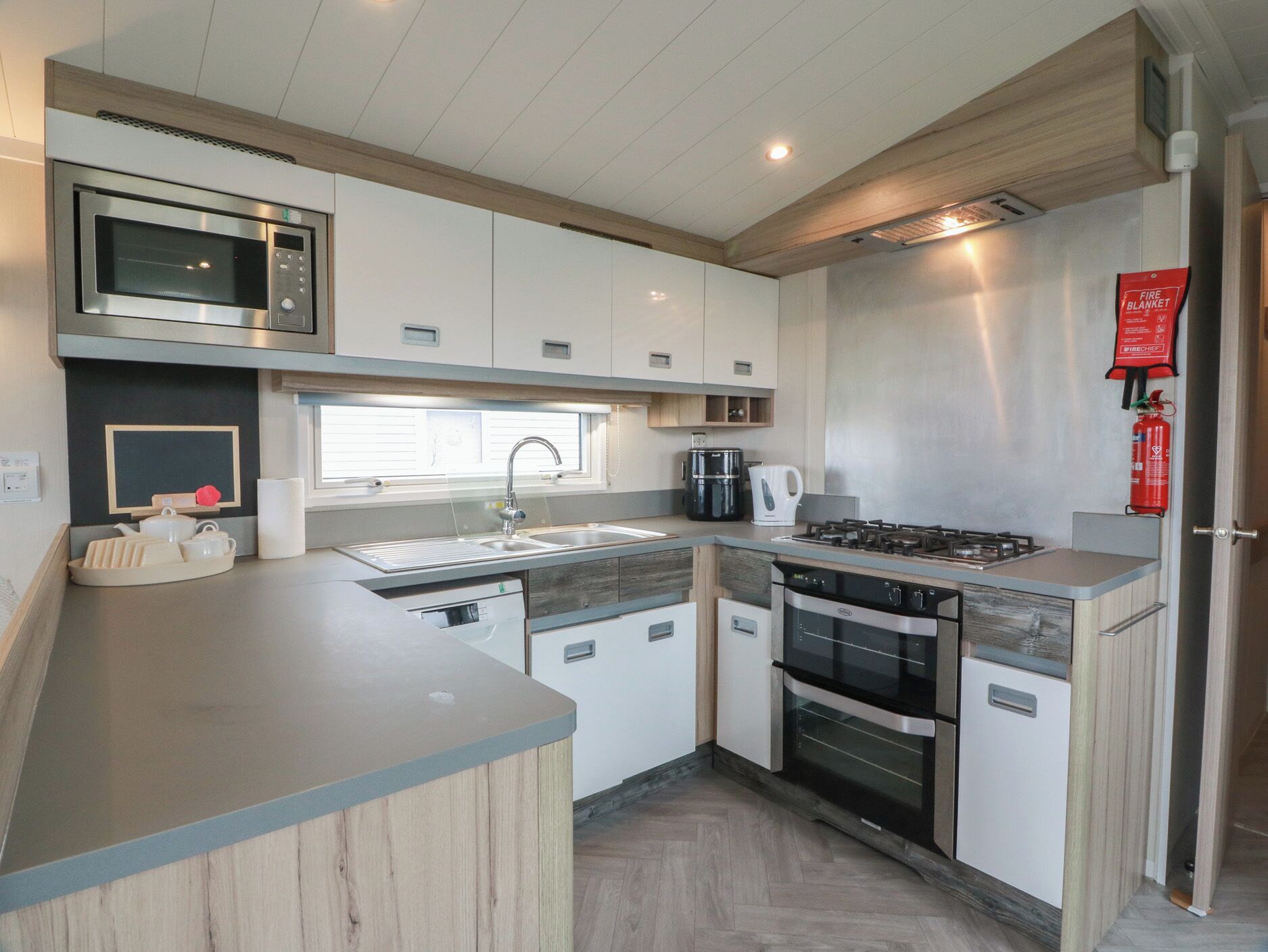 A modern kitchen with a built-in microwave, gas stove, oven, and a sink with a window above.
