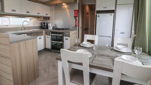 A compact kitchen with a sink, stove, and oven, a dining table with chairs, and a refrigerator. - Craig Tara Holiday Park 101 Bay View (Ayr)