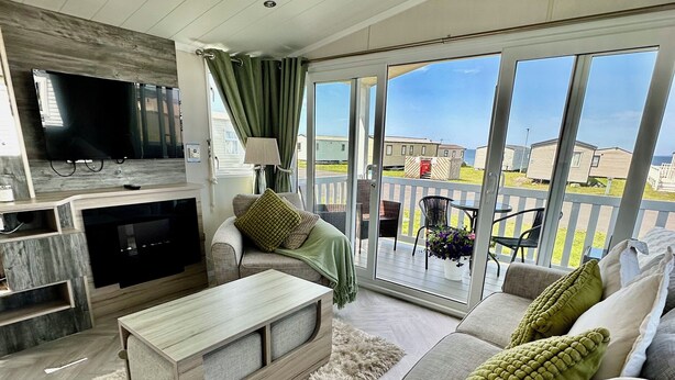 A spacious living room with a flat-screen TV, a wooden coffee table, and a sofa with green cushions. - Craig Tara Holiday Park 101 Bay View (Ayr)