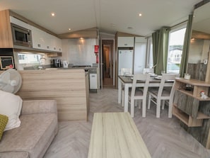 A compact kitchen with a microwave, stove, and sink. There is a dining area with a table and chairs, and a small seating area with a sofa.