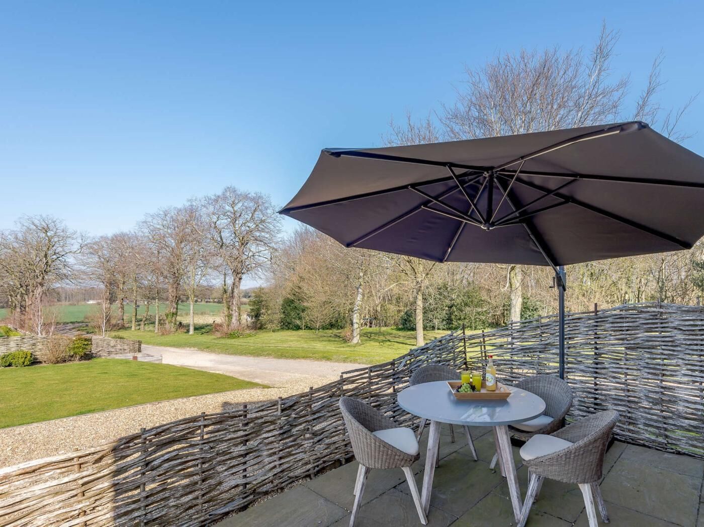Une terrasse extérieure avec une table ronde, des chaises en osier, un grand parasol et une vue sur un paysage rural.