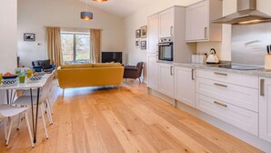 A modern kitchen with white cabinets, a stainless steel range hood, and a dining area with a yellow sofa and a table set for breakfast. - 2 Bed in Norwich (oc-87511) (Colby)