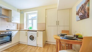 A compact kitchen with a washing machine, a dining area with a table and chairs, and a window providing natural light. - 1 Bed in Cockermouth (oc-87480) (Cockermouth)