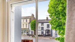 A window with a view of a street, a building with 'ALE & FOOD' signage, and a red vase in the foreground. - 1 Bed in Cockermouth (oc-87480) (Cockermouth)