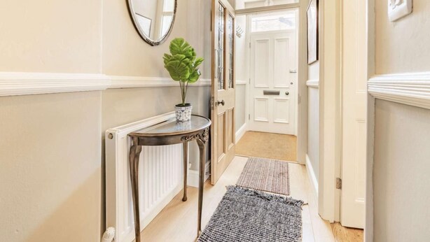 A hallway with a radiator, a round mirror, a potted plant, a console table, and a door leading to another room. - 2 Bed in Keswick (oc-87732) (Keswick)