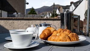 A table with a plate of croissants, a teapot, and cups, set outdoors with a mountain view in the background. - 2 Bed in Keswick (oc-87732) (Keswick)