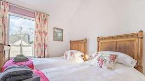 A double bed with floral bedding, a wooden headboard, a window with floral curtains, and a painting on the wall. - 2 Bed in Keswick (oc-87732) (Keswick)