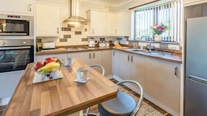 A modern kitchen with a wooden table, a fruit bowl, a kettle, and a refrigerator. - 2 Bed in Mablethorpe (oc-87801) (Mablethorpe)