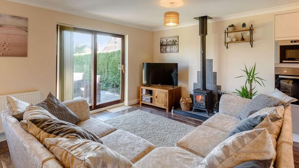 A living room with a sofa, TV, fireplace, and a sliding glass door to a garden. - 2 Bed in Mablethorpe (oc-87801) (Mablethorpe)
