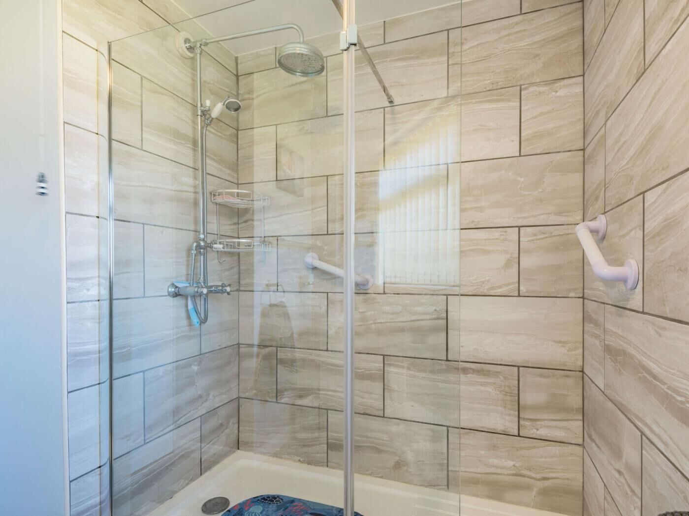 A glass-enclosed shower stall with a handheld showerhead, a wall-mounted towel rack, and a corner sink with a handheld faucet.