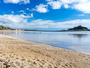 Ein Strand mit Kieselsteinen, ruhigem Wasser, weit entfernten Hügeln und einem schlösserartigen Bau.
