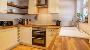 A modern kitchen with white cabinetry, a built-in oven, a coffee maker, and a window with a plant. - 2 Bed in Lowestoft (oc-88109) (Lowestoft)