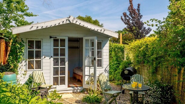 A small, white wooden structure with multiple windows, a door, and a bench outside. - 2 Bed in Lowestoft (oc-88109) (Lowestoft)