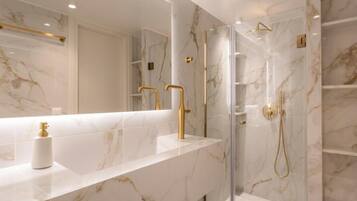 A modern bathroom with a marble countertop, gold fixtures, and a glass-enclosed shower.