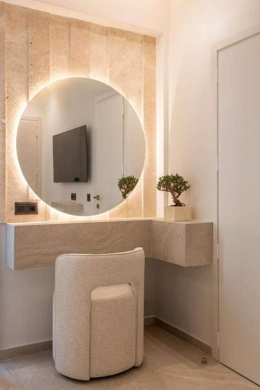 A modern bathroom with a round mirror, a flat-screen TV, and a small potted plant.